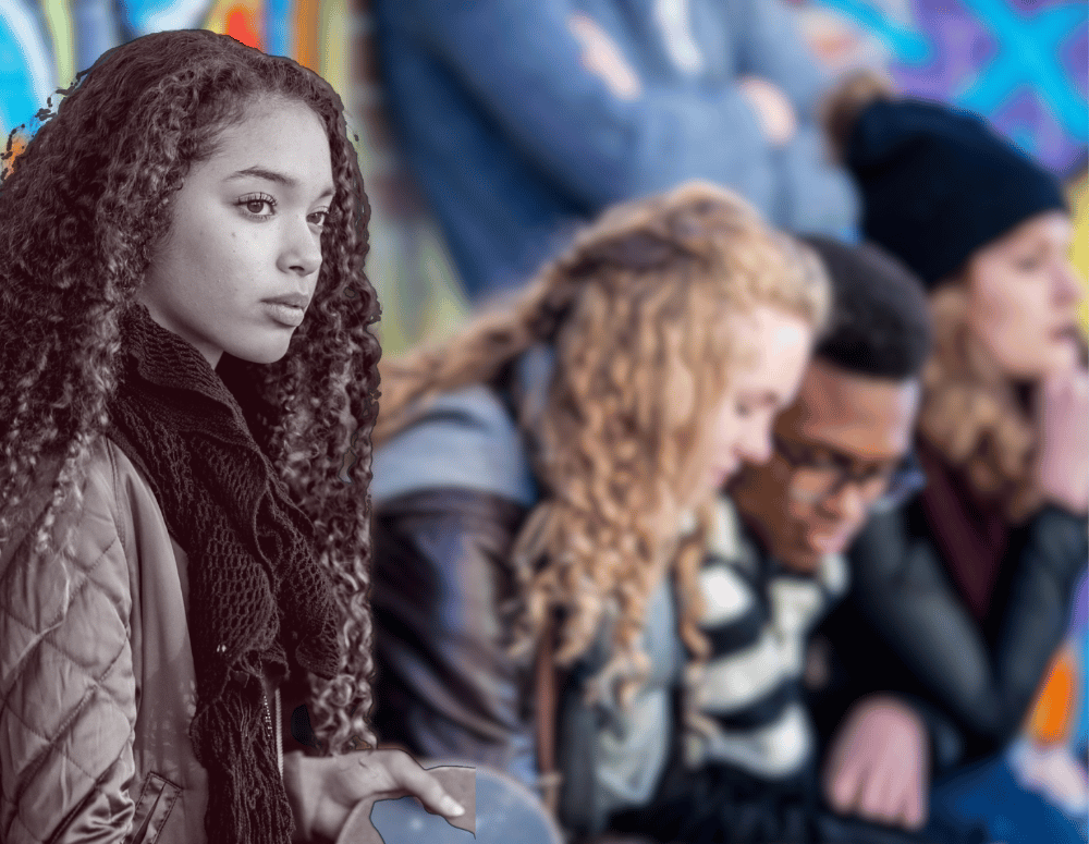 Teen girl with skateboard looking wistful while a group of teens talks behind her